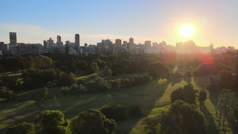 Carretilla-Aérea-En-El-Campo-De-Golf-Municipal-Verde-En-El-Barrio-De-Palermo-Con-Edificios-En-El-Fondo-Al-Atardecer,-Buenos-Aires