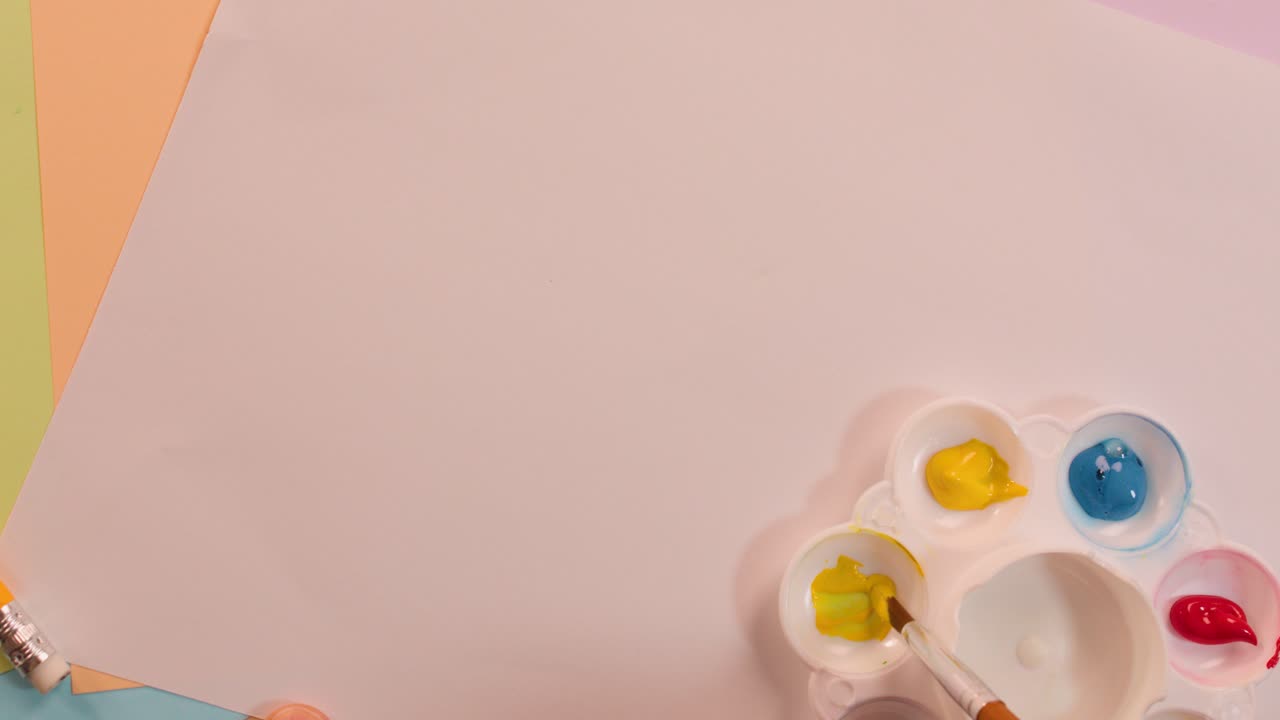 Artist arranges blue, yellow, red paint in palette on pastel desk under soft lighting