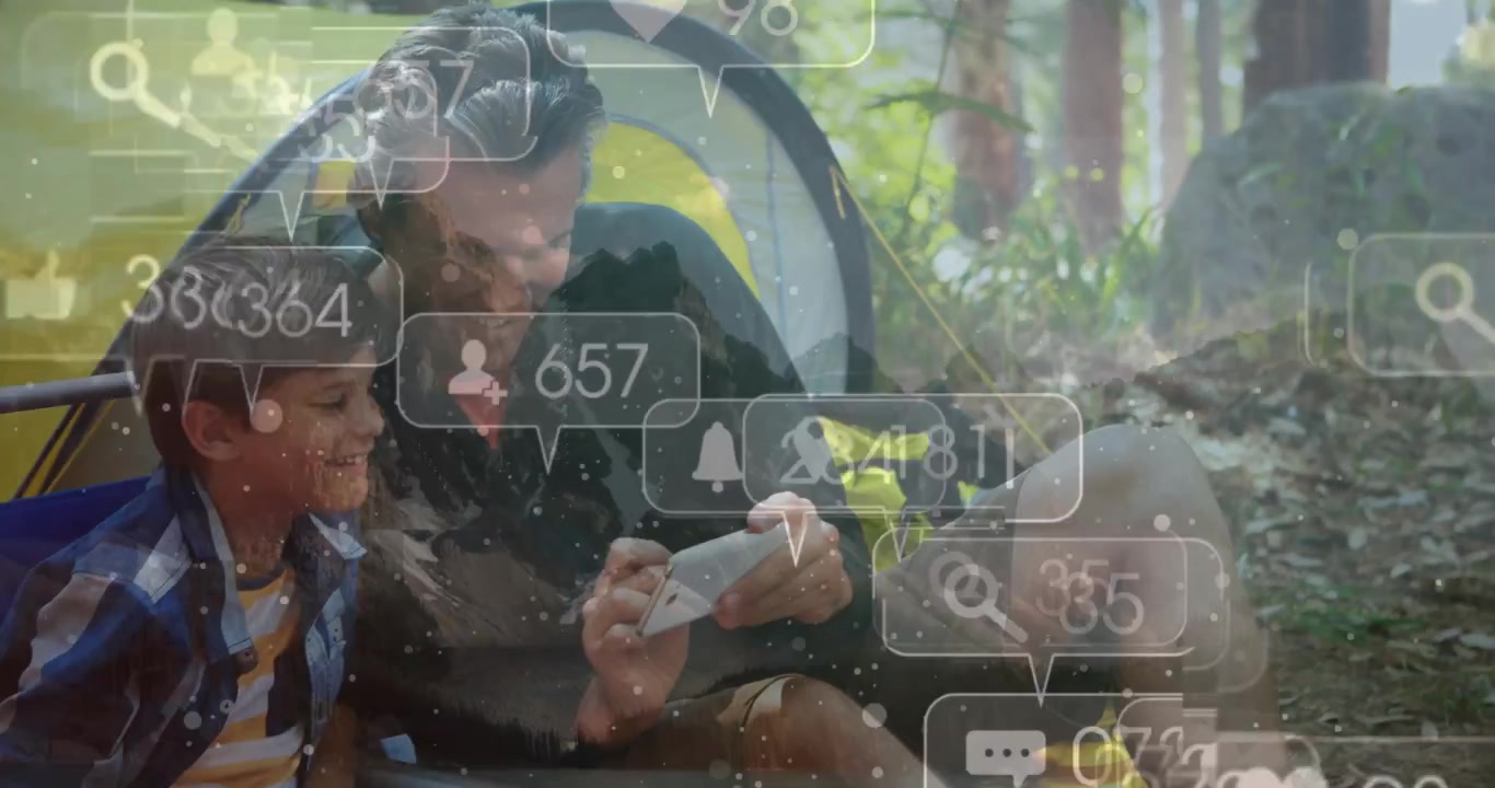 Papà che tocca lo smartphone e condivide contenuti social con un bambino vicino a una tenda gialla mentre bolle fluttuano