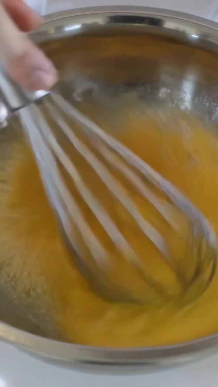 Video verticale: Una mano che entra tenendo una frusta che mescola un composto di uova in una ciotola d'acciaio sul bancone, aerando.
