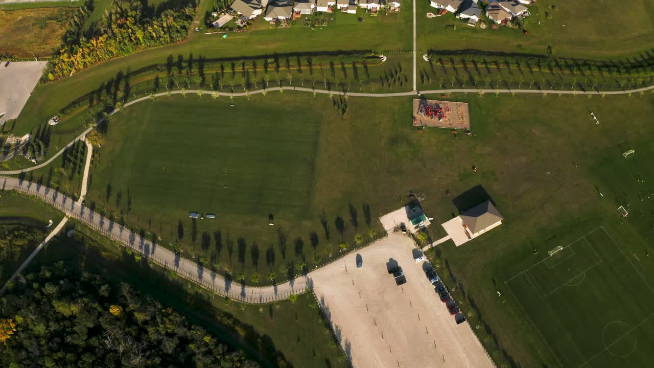 Top down dolly right 4k shot of a beautiful lush green soccer park with walking paths and play structures nearby