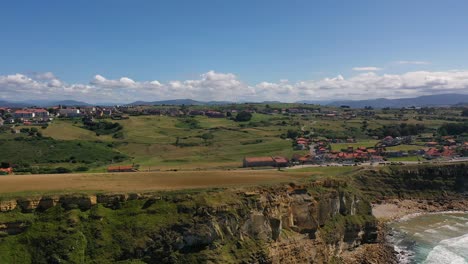 lateral flight on a cliff with a background of mountains there are population centers with scattered houses with green land on the coast we discover a beach with waves at sunset in cantabria spain