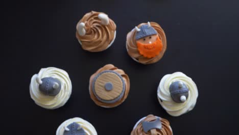 Topdown-motion-over-Viking-theme-cupcakes-on-Black-table,-Rack-focus