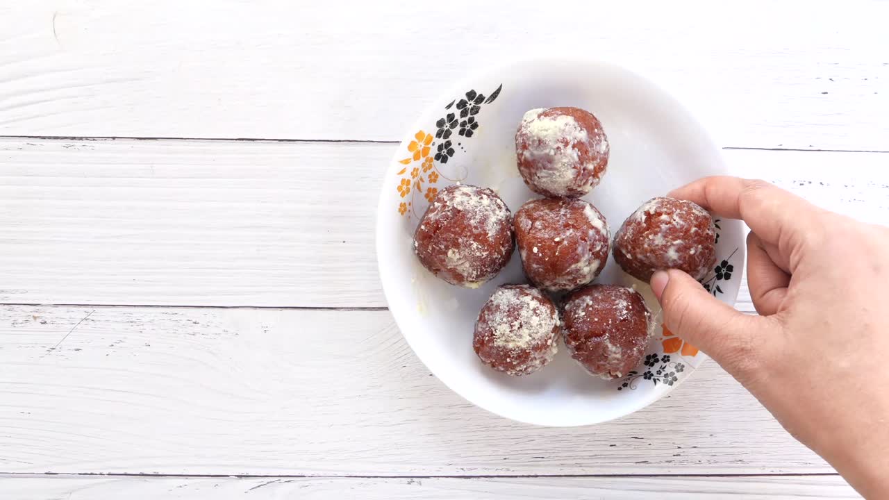vista superior de la mano de la mujer recogiendo dulces indios de un cuenco en la mesa.