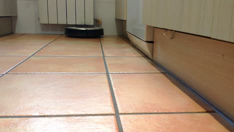 a hoovering robot is going through the kitchen floor made of tiles