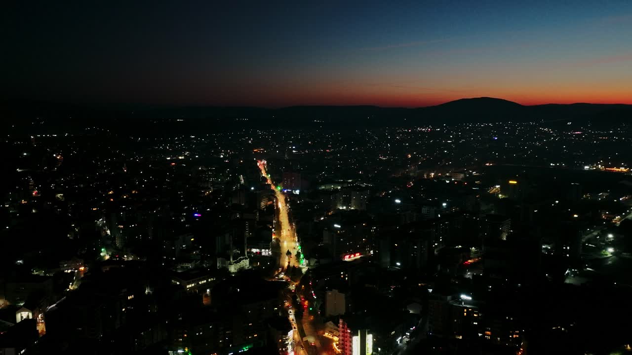 Twilight horizon fades as city lights brighten beneath fast circling drone view