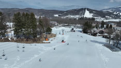 Slow-tracking-shot-flying-down-mountain-following-cable-car-chair-lift,-skiers-skiing-down-the-slopes-below