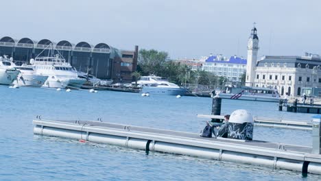 person sitting on a dock in a marina, with boats and city in the background