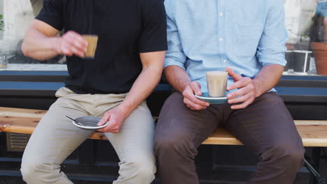 close up of two men sitting outside coffee shop drinking coffee