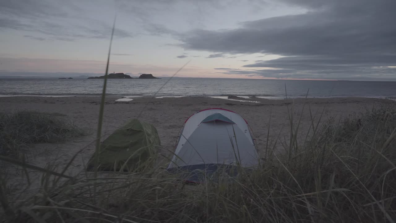 Wild camping in a beach in scotland. Two tents in fornt of the sea during sunrise time. Wide angle shot and green vegetation