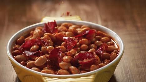 red pepper is being thrown on the bean dish with pastrami in slow motion.