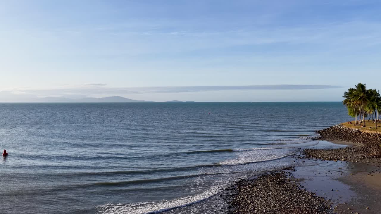 Drone captures serene coastal landscape with mangroves, pier, and ocean waves under clear skies in Port Douglas, Queensland