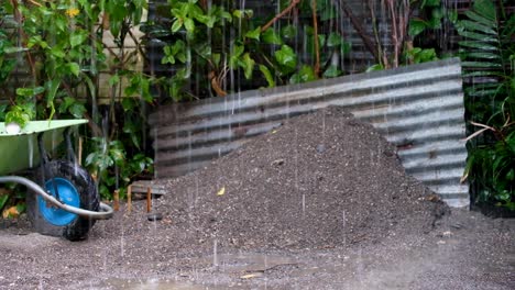 un montículo de grava gris, chapa y una carretilla verde en el sitio de construcción durante un aguacero húmedo y lluvioso