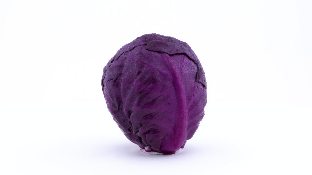 una mini repollo púrpura entera está girando en la mesa giratoria. gotas de agua aparecen en la piel durante la rotación. aislados en el fondo blanco. primer plano. macro.