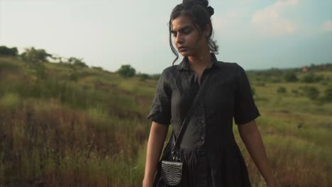 toma cinematográfica de una mujer morena con un vestido negro posando en un campo