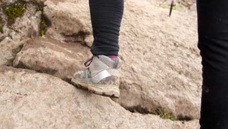 rear view of a female tourist's leg in trekking boots climbing up the rocks with trekking poles.