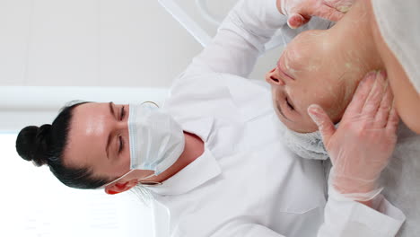 cosmetologist applying moisturizing medical chemical peeling cream mask on young adult woman face