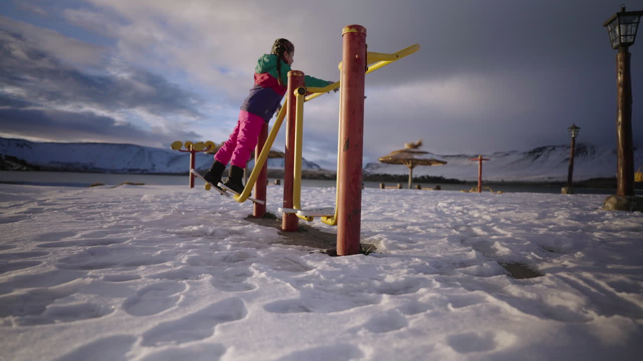 Girl in vibrant winter outfit playing at outdoor fitness park in snowy setting