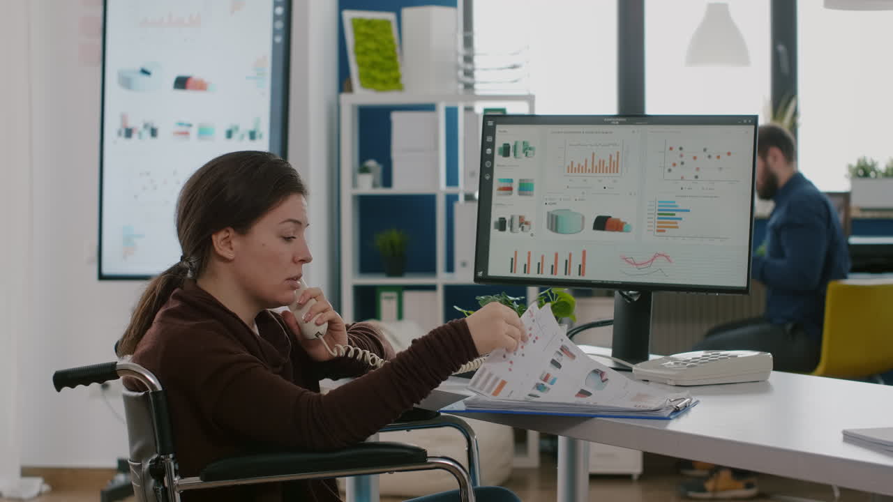 emprendedor discapacitado ocupado hablando por teléfono con un colega revisando gráficos