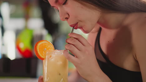 attractive woman drinks cocktail through straw in bar. seductive lady refreshes with exotic alcoholic drink resting in nightclub. pretty party guest