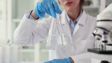 a scientist in a lab coat and gloves holds an erlenmeyer flask with liquid in a laboratory