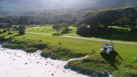 aerial view guy sitting on his land rover with surfboard leaning against the car looking out to the surf