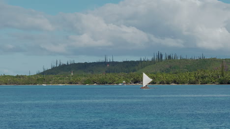 handmade kanak pirogue with triangle sail floats in upi bay near isle of pines