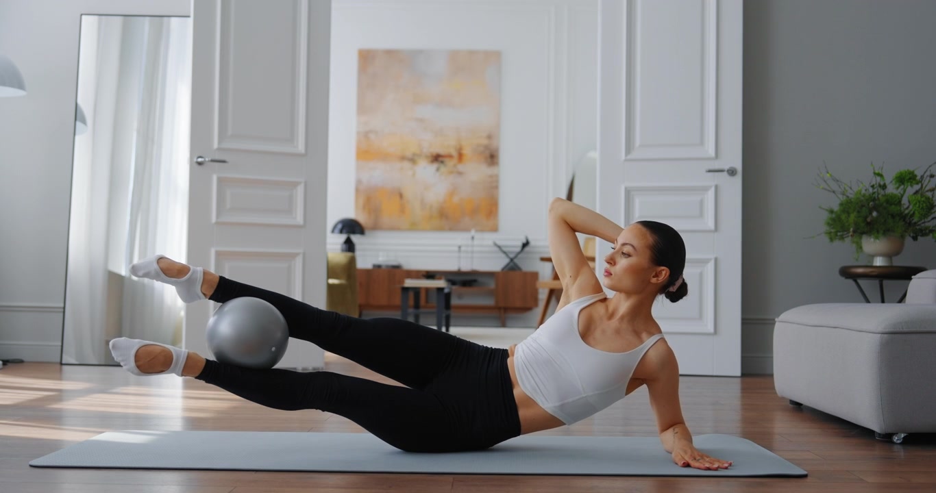 Young Woman Performing Pilates Leg Raises with Small Ball at Home