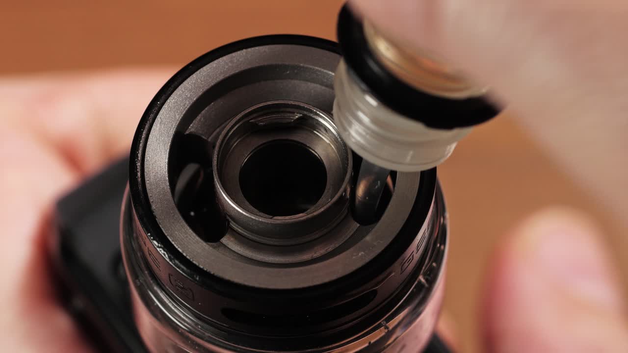 Primer plano de un gotero llenando un tanque de vapeador con e-líquido a través de la abertura superior.