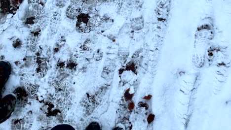 Pov-top-down-of-person-with-walking-boots-hiking-on-snowy-path-with-many-shoeprint-of-other-hiker