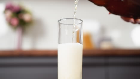 pouring creamy beverage into a tall glass, partial view of hand with bottle, reflected surface