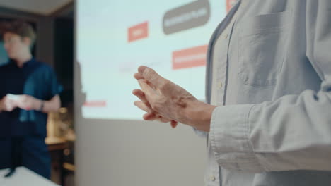 hands of businesswoman gesturing when giving presentation on office meeting, projection screen and female colleague in the background. close-up impersonal shot