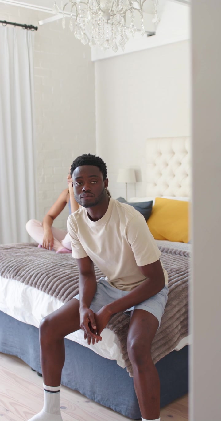 Video verticale: Coppia afroamericana a letto, donna in canottiera che alza le mani parlando, uomo che ascolta.