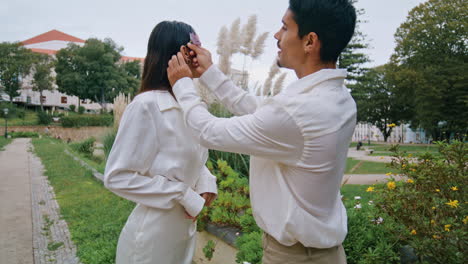 stylish lovers walking garden. latina gentle man putting flower behind woman ear