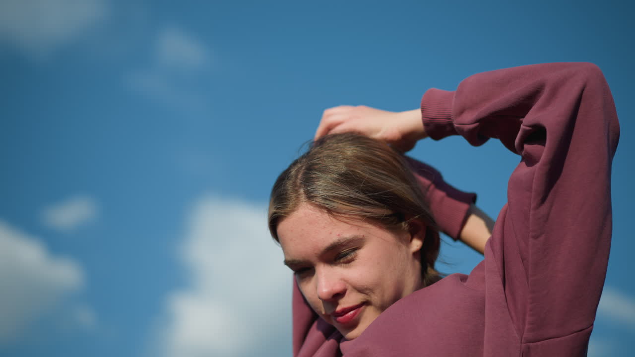 은 하늘 아래 빛이 그녀의 얼굴을 강조하는 동안 따뜻한 미소로 피트니스 운동에 참여하는 운동선수, 머리 위에 팔을 펴고, 그녀는 집중하고 편안해 보입니다.