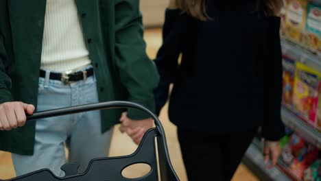 Cropped-footage-of-mother-and-daughter-in-supermarket-pushing-the-cart-and-holding-hands