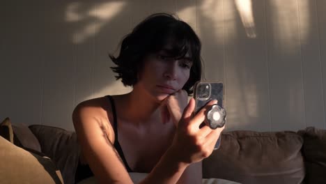 Girl-illuminated-by-sunlight-sitting-on-sofa-while-looking-at-smartphone