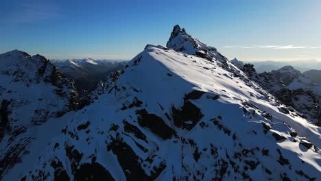 Aerial-rising-shot-of-snowy-mountains-in-Norway-with-icy-peak-and-blue-sky-in-winter