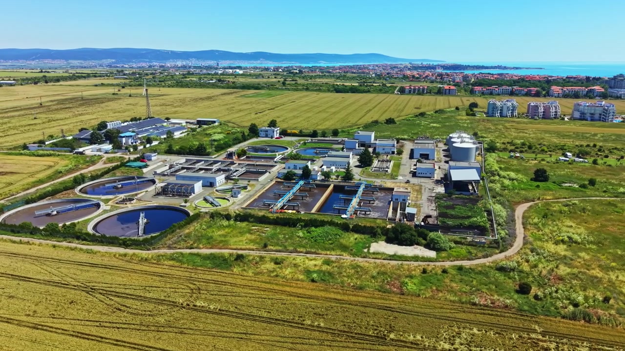 Water treatment facility located in a rural area with fields and buildings visible under clear sky during daytime