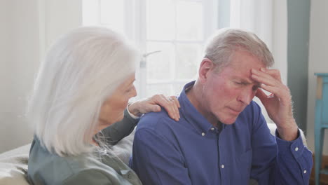 woman sitting on sofa comforting senior man suffering with mental health issues at home