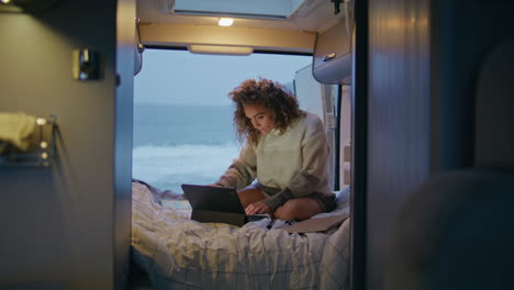 serious freelancer working camper van looking laptop at evening. woman surfing