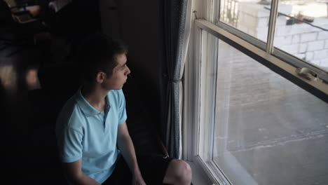 a young man, teenage boy, suffering from depression, anxiety and mental health issues looks outside of window