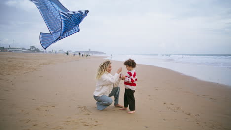 mom playing kite kid at windy seashore. caring parent helping son launching toy.
