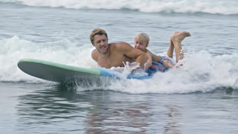 excited boy riding with father on surfboard in ocean