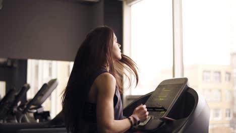 Attractive-brunette-girl-with-long-hair-in-her-20's-wearing-dryfit-sportswear,-running-on-treadmill.-Indoors-footage.