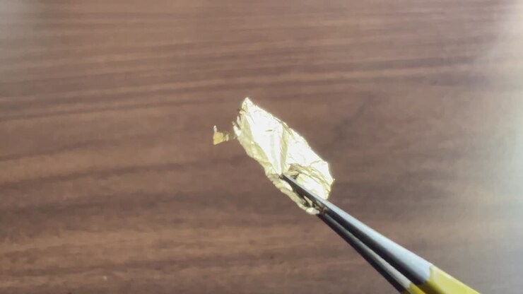 Close up fixed shot of gold leaf foil being held in fine pointed tweezers
