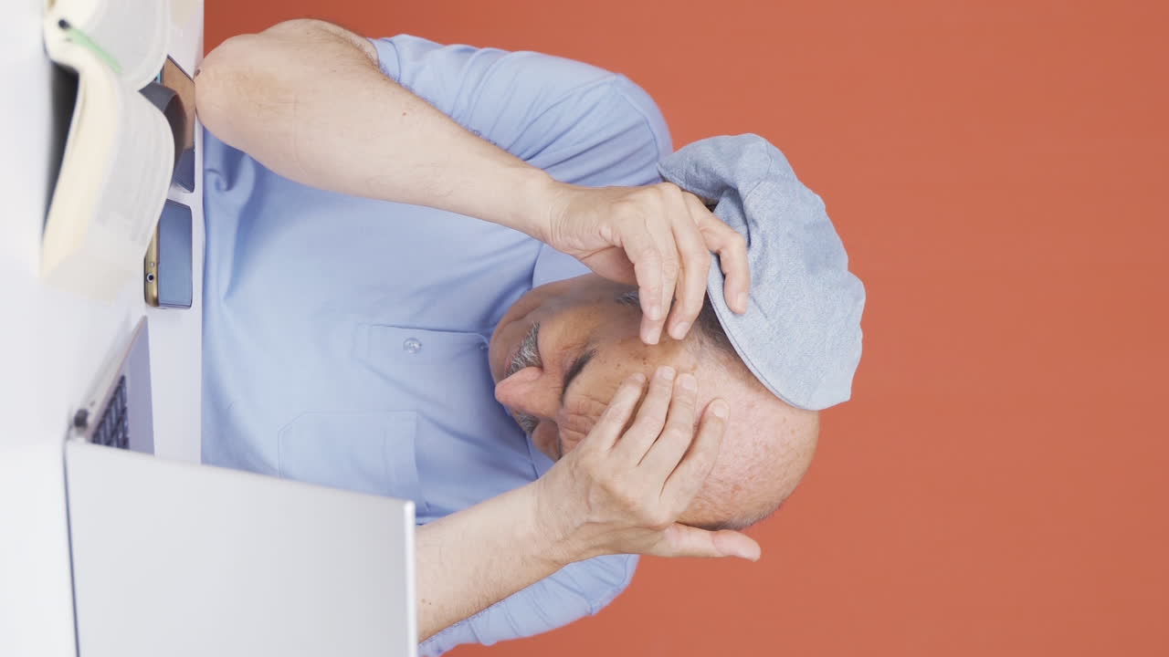 el video vertical del anciano trabajando en la computadora portátil tiene dolor de cabeza.