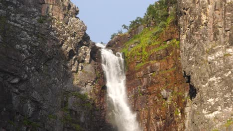 Medium-close-up-tilt-up-shot-of-Njupeskär-waterfall,-plunging-fresh-water-between-eroded-canyon,-lit-by-midsummer-morning-golden-sun-at-Fulufjället-National-Park,-in-Särna,-Sweden