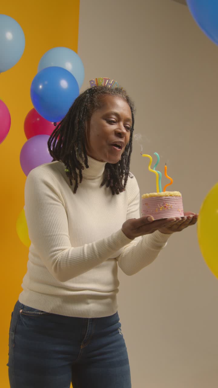 fotografía de estudio de video vertical de una mujer con una cinta para la cabeza de cumpleaños celebrando su cumpleaños soplando velas en el pastel 1