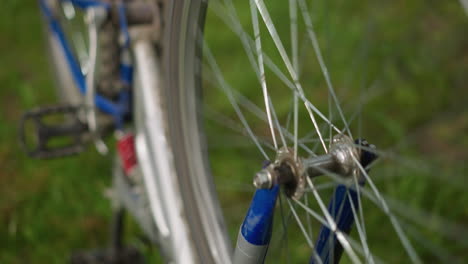primer plano de una bicicleta colocada al revés con su neumático trasero girando lentamente, el enfoque está en la rueda y los radios, mientras que el fondo de la vegetación permanece suavemente borroso